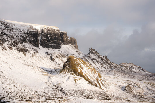 View of snow-covered mountains with rocky outcrops piercing the white blanket under a cloudy sky, creating a stark, dramatic landscape, Quiraing, Isle of Skye, Scotland.