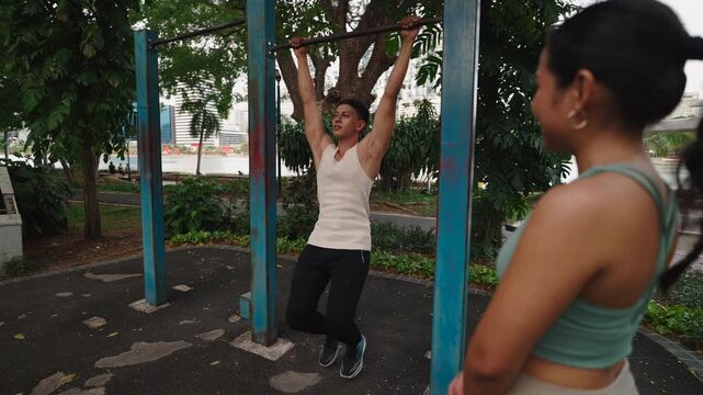 Young Latin American and Young Asian Mgirl Doing A Leg Curl Exercise Hanging From A Bar In The Park