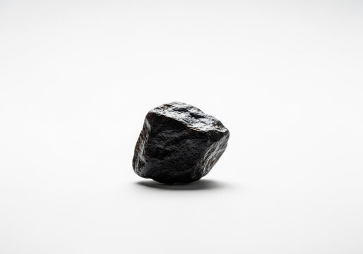 A single, rough, dark, natural shilajit resin rock isolated on a clean white background, showcasing its raw, mineral-rich texture and organic form in a minimalist studio shot.
