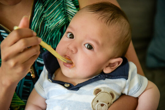 young baby eating applesauce in his mother's arms
