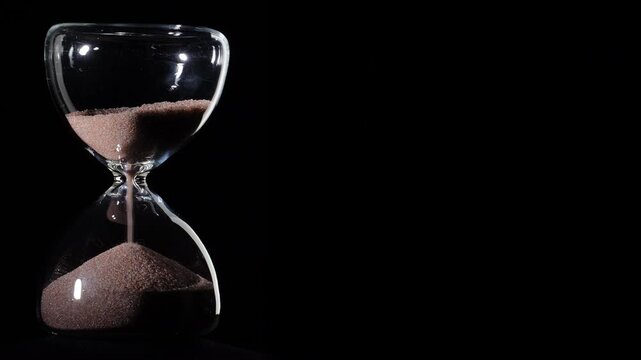 Hourglass flowing on black background. Left align composition with copy space on right, time management concept, minimalist product shot, hourglass in motion, clean style, last grains of sand
