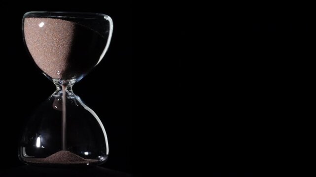 Hourglass flowing on black background. Left align composition with copy space on right, time management concept, minimalist product shot, hourglass in motion, clean style, starting to flow
