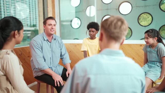 Smart teacher talking about mental health problem and sharing idea with boy during group therapy. Happy instructor pointing at children while explain plan while student listening idea. Edification