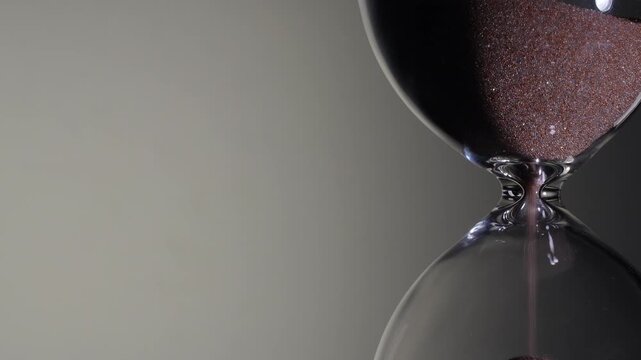 Macro of sand pile rising in hourglass neck on white background. Close up of sandglass, rising sand pile. Left copy space, time is up concept, deadline approaching, minimalist product shot.