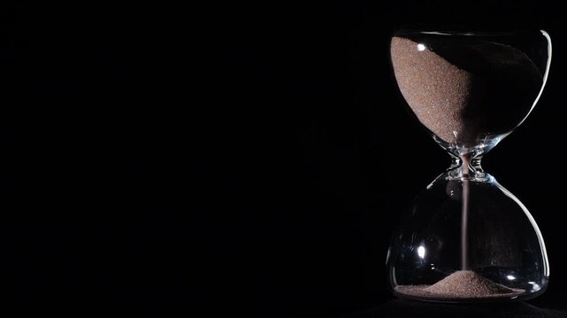 Hourglass flowing on black background. Right align composition with copy space on left, time management concept, minimalist product shot, hourglass in motion, clean style, starting to flow
