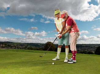 Fototapeta premium Two senior female golfers being coached on putt on golf course