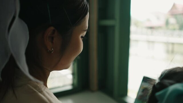 Young woman using laptop computer for studying while sitting by the window