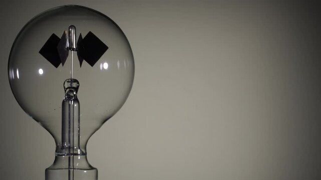 Left align, rotating Crookes radiometer light mill on bright white background. Black start. High-key lighting, minimalist science experiment, solar vane, physics education, right copy space