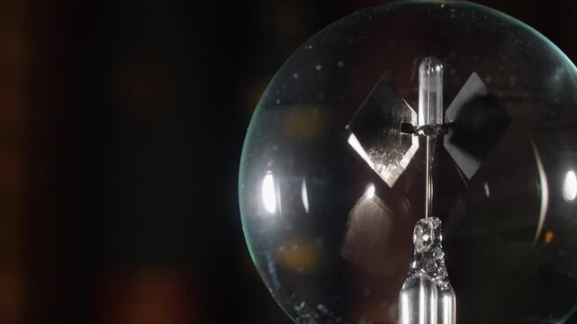 Extreme close up marco of rotating right align Crookes radiometer light mill with gold reflections on bookshelf background, start-stop motion, cinematic warm lighting, left copy space,