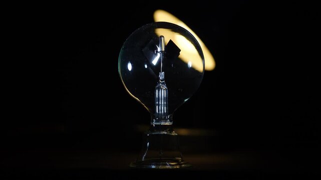Rotating Crookes radiometer light mill with warm backlighting on black background. Center aligned comp with Left-Right copy space, physics, solar vane, cinematic lighting, start-stop motion