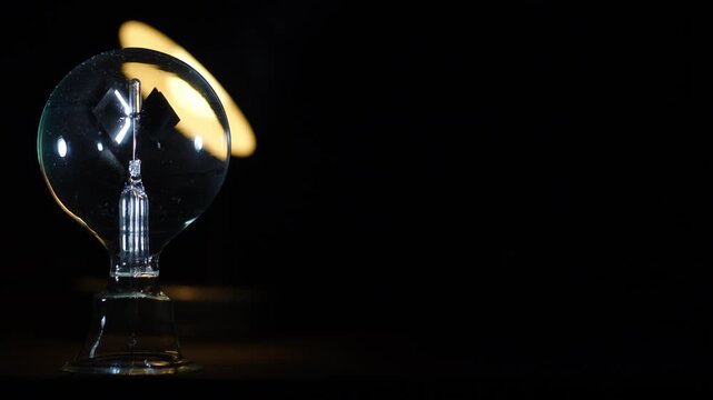 Rotating Crookes radiometer light mill with warm backlighting on black background. Left aligned composition with copy space, physics experiment, solar vane, cinematic lighting, start-stop motion