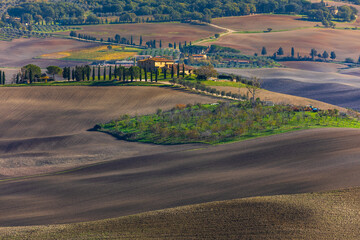 Naklejka premium Tuscan countryside with rolling cultivated fields and traditional farm, Italy.