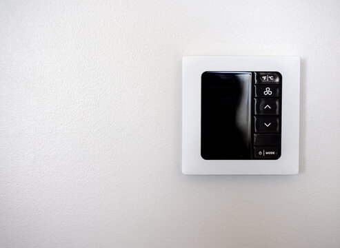 Modern wall mounted thermostat control panel on white wall
