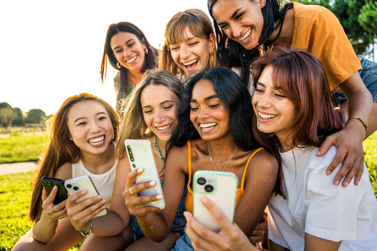 Multiracial young women using smart mobile phone device at the park - Happy female friends watching funny video on smartphone - Trendy modern technology life style concept
