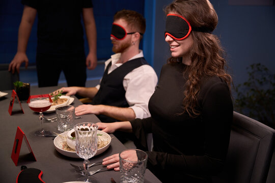 Two seated adults enjoying blindfolded dining experience indoors