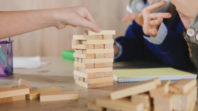 Children play a stacking game with wooden blocks at a table during a group activity in a classroom setting in the afternoon