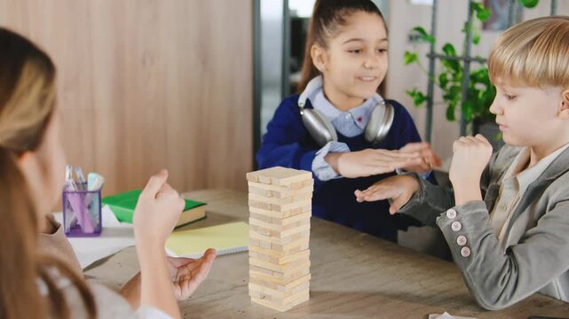 Children play Jenga on a table in a classroom while focusing on their moves and enjoying the activity during the day