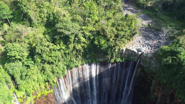 Stunning panoramic drone shot of Tumpak Sewu waterfall surrounded by green forest.