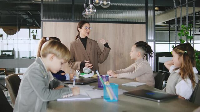 Group of children learning and discussing ideas in a modern classroom setup with a teacher at a large table in the daytime