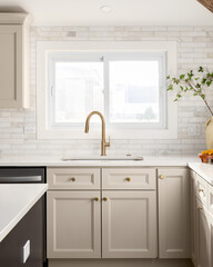A kitchen detail with brown cabinets, marble subway tile backsplash, gold faucet, and decorations on the marble countertop.