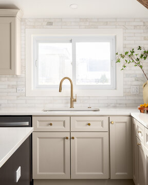 A kitchen detail with brown cabinets, marble subway tile backsplash, gold faucet, and decorations on the marble countertop.