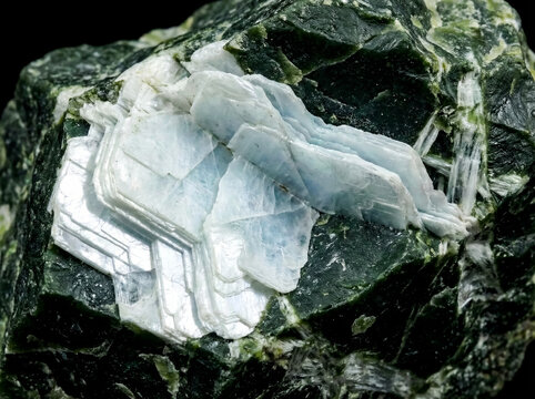 Pale blue platy brucite crystals forming a layered aggregate on a dark green serpentinite rock matrix.