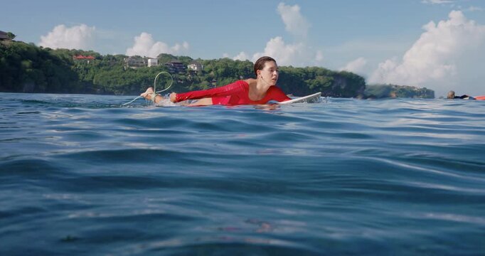 Surfer woman paddling on surfboard in red swim suit. Surfing process
