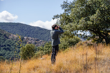 Obraz premium Young man looking at the horizon with binoculars in the forest