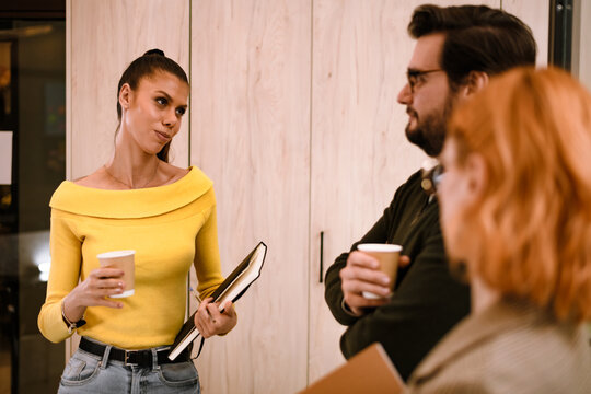 Group discussion with a woman in a bright yellow top holding a notebook as two colleagues participate in a productive meeting at a modern office in the afternoon