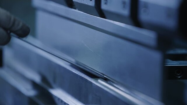 Slow motion close up of worker hands bending metal sheet on press brake in industrial factory workshop.