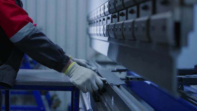Worker operating metal press brake bending sheet metal in industrial workshop with steady close movement along machine.