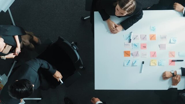 Top view of investor writing white board to present project and putting hand together with professional business team to celebrate successful project at meeting table with sticky note. Directorate.