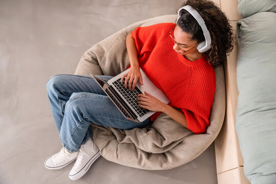 Woman relaxing on bean bag with laptop and headphones