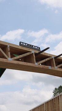 Construction site forklift telehandler lifting wooden trusses beams into place under clear blue sky.