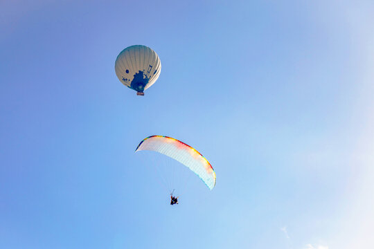 Paraglider and hot air balloon soaring in blue sky