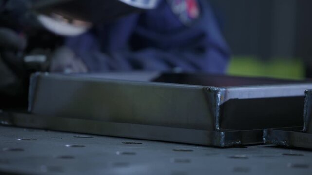 Slow motion welder welding sparks hitting metal box on workshop bench during fabrication..