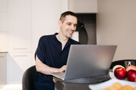 Man smiling while working on laptop in bright kitchen