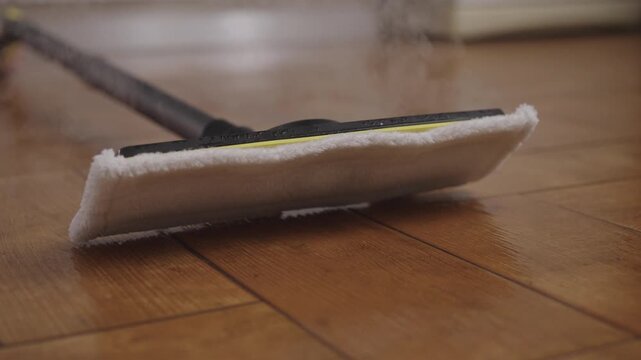 Steam mop resting after cleaning wooden floor, emitting hot vapor for effective sanitization and deep cleaning, ensuringa sparkling and hygienic home environment.