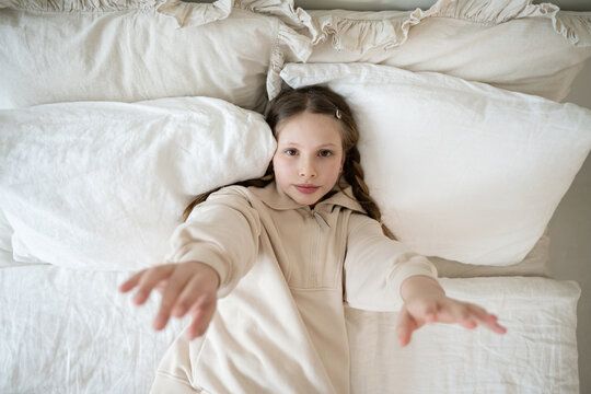Girl lying in white bed with arms extended forward