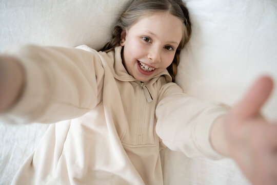 Girl lying in white bed with arms extended forward