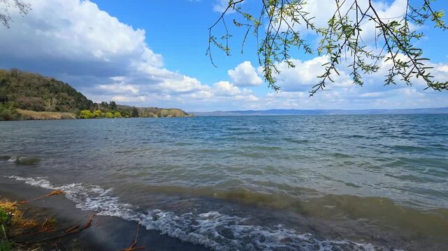 Panoramic view of Lake Bolsena with dark volcanic sand beach, wavy blue water and dramatic cloudy sky in Lazio, Italy