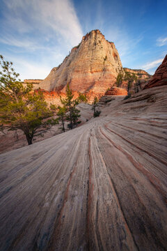 View of the striated rock formations leading to the towering sandstone peak kissed by the sun's rays, showcasing Zion's natural beauty, Springdale, Utah, United States.