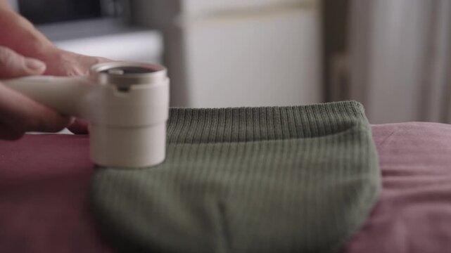 Person using depilling machine, removing lint and fabric balls from knitted beanie, essential part of clothing and textile care for garment longevity. Concept of effective fabric care.