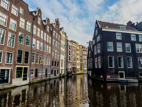 View of historic brick buildings mirroring in the still canal waters under a patchy blue sky, a tranquil scene of old-world charm, Amsterdam-centrum, Noord-Holland, Netherlands.