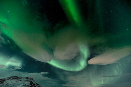 View of ethereal green auroras dance and swirl above the snow-dusted ground, painting the night sky with vibrant hues, Northern Lights, Reykjanes Peninsula, Iceland.