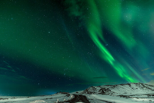 View of vibrant green and blue Northern Lights dance across the Icelandic night sky above a snowy landscape, Northern Lights, Reykjanes Peninsula, Iceland.