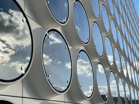 View of the building's facade, with round windows reflecting the sky, creating a contrast between the white facade and the blue sky, Amsterdam, Netherlands.