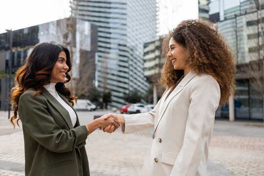 Women shaking hands outside office buildings
