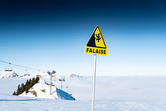 View of a stark yellow warning sign against a backdrop of snow-covered peaks and a soft blanket of clouds, Val-d'Illiez, Valais, Switzerland.