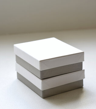 Two minimalist white boxes with gray bases placed neatly on a white table, creating a clean and modern composition. Ideal for packaging design, branding, product presentation, and mockup concepts.